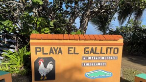 Schild für Playa El Gallito mit einem Hahnen-Logo und der Aufschrift 'The Little Rooster' und 'Le Petit Coq'.