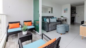 Een modern appartement met balkon, een grijze zithoek, een eethoek en een keuken die door een open deur zichtbaar is.