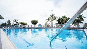 Ein Schwimmbecken mit klarem, blauem Wasser, umgeben von Palmen und einem weißen Zaun.