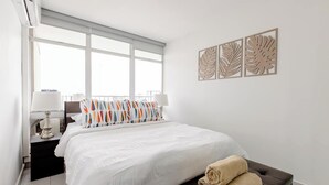Ein Hotelzimmer mit einem großen Bett, einem Nachttisch mit Lampe, einem Fenster mit Jalousien und drei Wandbildern.
