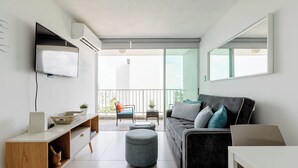 Ein modernes Wohnzimmer mit Sofa, Hocker, Fernseher und einem Balkon mit Stuhl und Tisch.