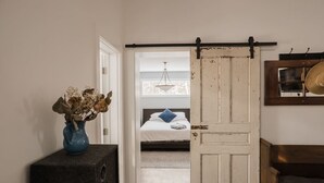 Un pasillo que conduce a un dormitorio con una cama, un jarrón con flores secas y una puerta rústica.