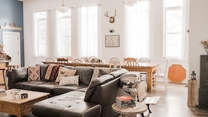 Amplia sala de estar con un sofá modular, una mesa redonda y un comedor con mesa de madera y sillas.