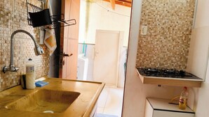 Une cuisine équipée d’un évier, d’un robinet et d’une cuisinière. Une bouteille d’huile de cuisson se trouve sur le plan de travail.