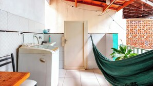 Une cuisine compacte équipée d’un lave-linge, d’un évier et d’une porte donnant sur un balcon avec un hamac et des plantes en pot.