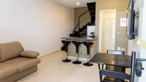 Una cocina moderna con estufa integrada, un comedor con mesa y sillas, y una escalera que sube a un nivel superior.