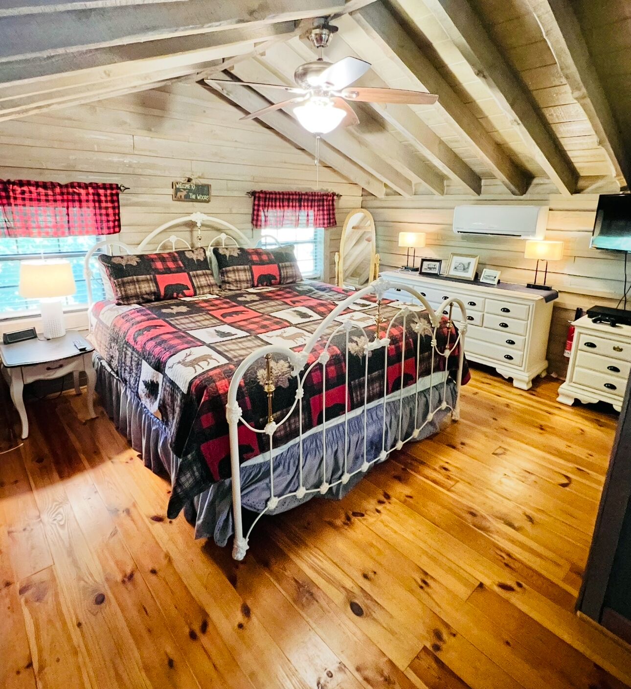 A cozy bedroom with a bed, wooden floor, ceiling fan, and a window with plaid curtains.