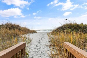 A wooden pathway leading to a beach with sand and sparse vegetation on either side. - Oceanfront Barefoot Serenity (Myrtle Beach)