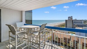Un balcon avec une table et des chaises, donnant sur une plage et offrant une vue sur la ville.