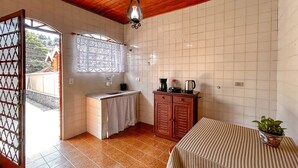 Uma cozinha compacta com pia, uma janela com cortinas de renda, um armário de madeira e uma mesa com toalha listrada.