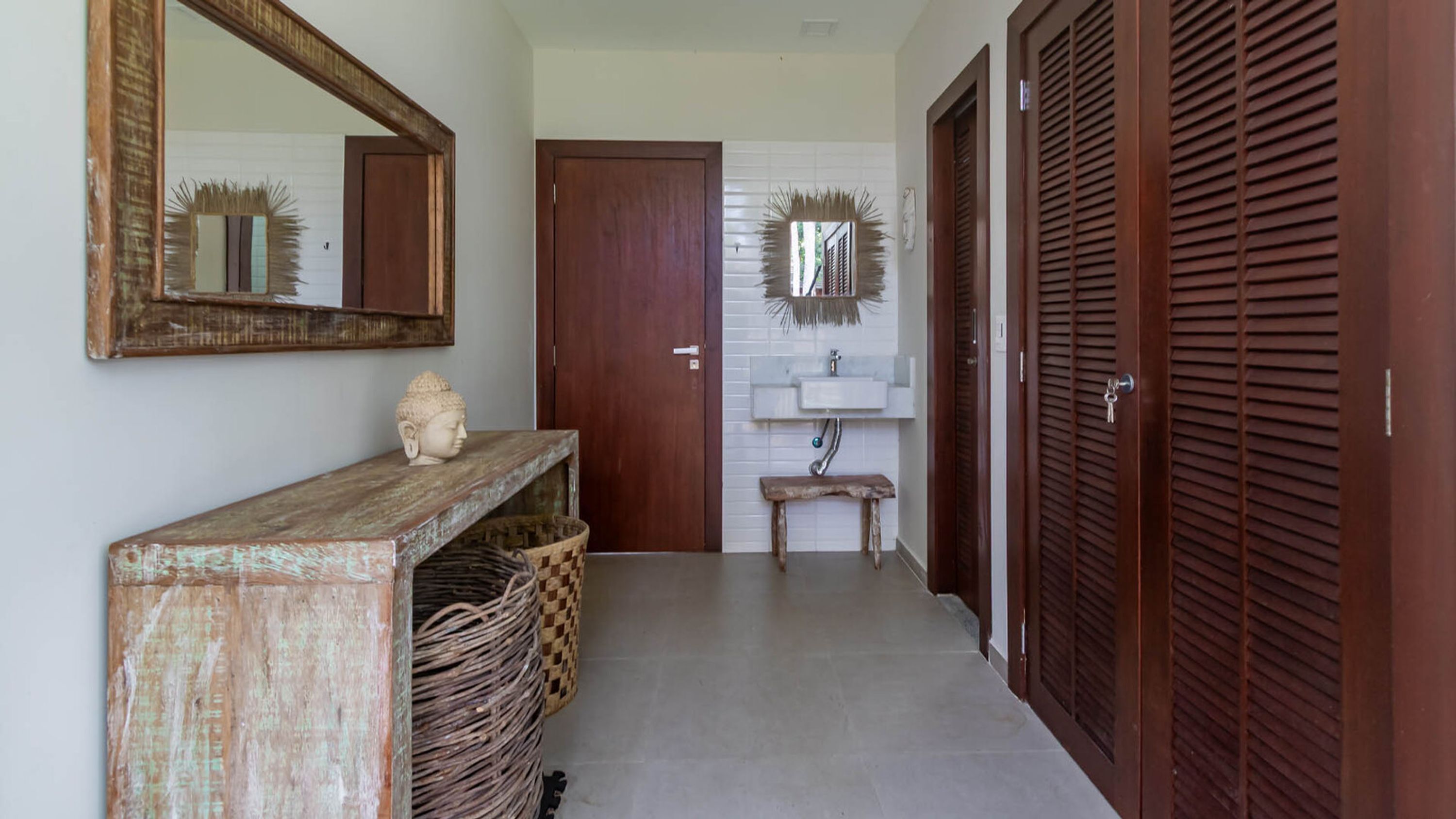 Un couloir avec une console en bois, un miroir, une porte, un lavabo et une porte en bois dotée de panneaux à persiennes.