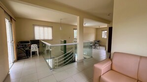 A spacious living area with a glass staircase, a dining area with a table and chairs, and a beige sofa. - Casa com Piscina Churrasq Wi Fi pr Ximo ao mar (Ipojuca)