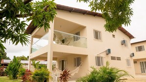 A two-story building with a balcony, multiple windows with bars, and air conditioning units. - Casa com Piscina Churrasq Wi Fi pr Ximo ao mar (Ipojuca)