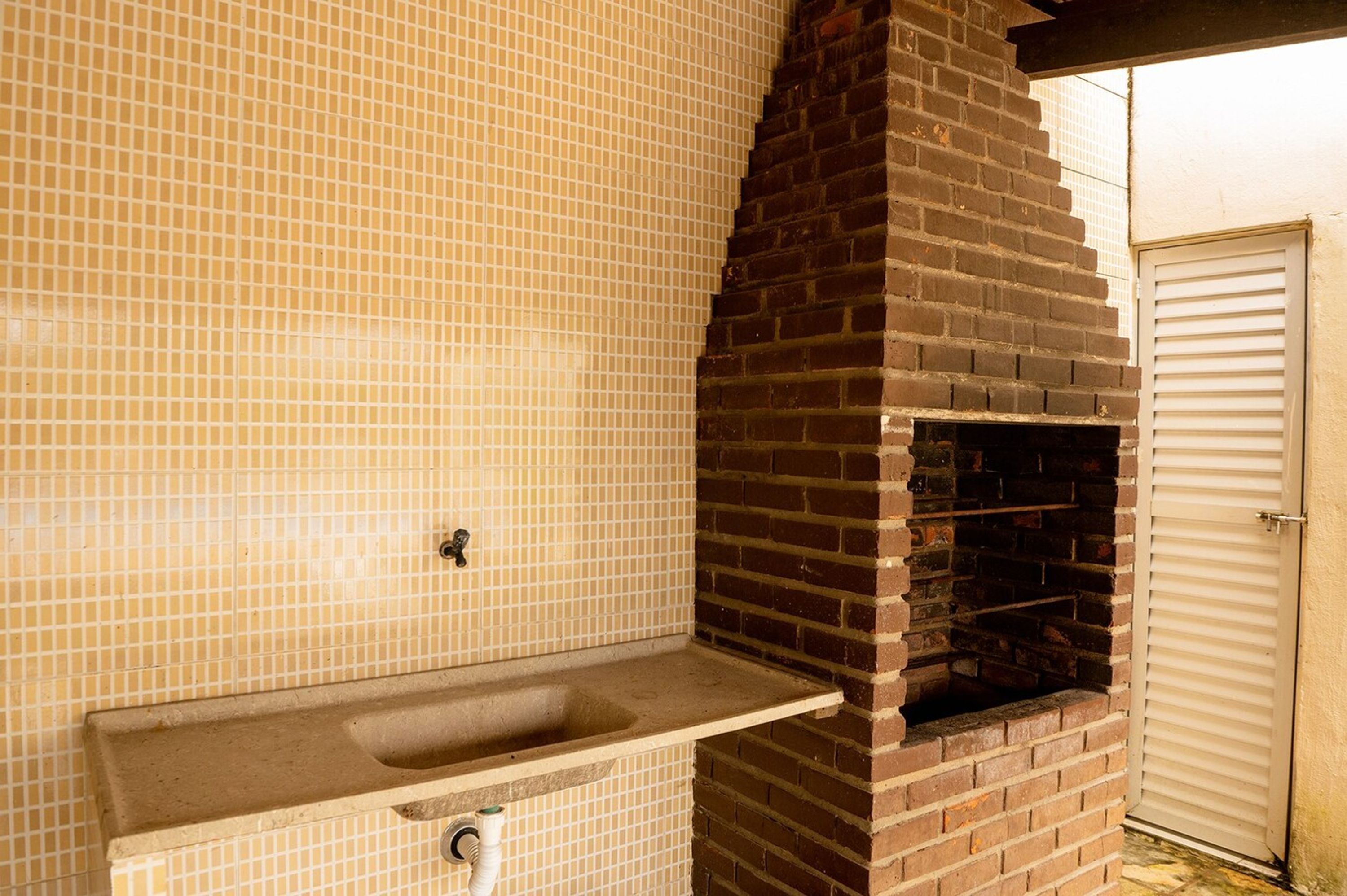 A kitchen with a tiled backsplash, a brick oven, and a sink with a pipe.