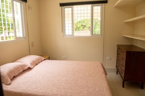 Ein Schlafzimmer mit einem Bett, einer Kommode und einem Fenster mit Blick auf Grünflächen.