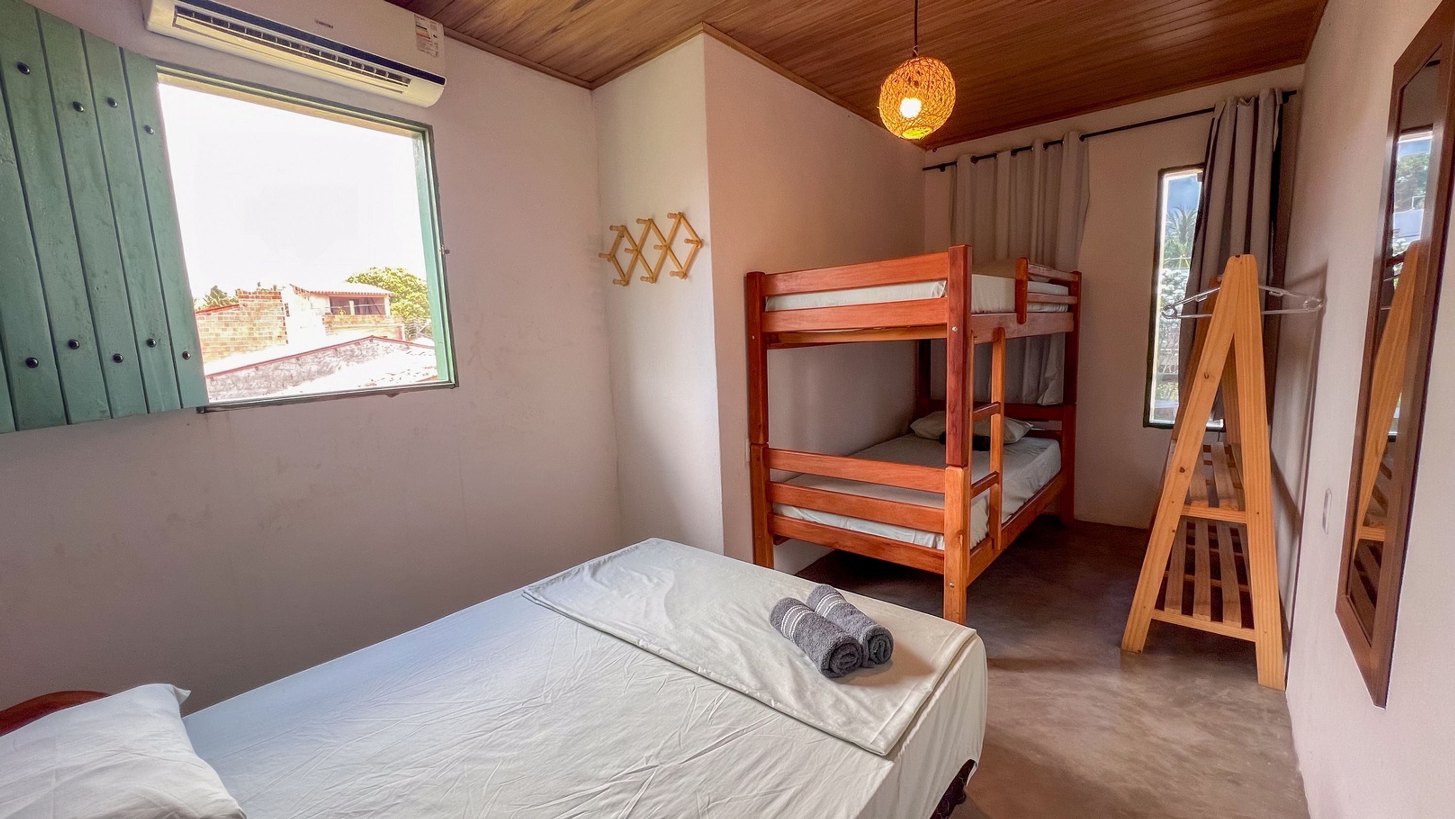 A room with bunk beds, a single bed, a window with shutters, a hanging light fixture, and a wooden ladder.