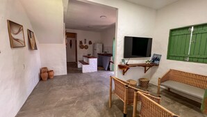 A living room with a TV, wicker furniture, and a kitchen in the background. - Casa Brisa das Guas Piscina e Churrasqueira (Porto de Pedras)
