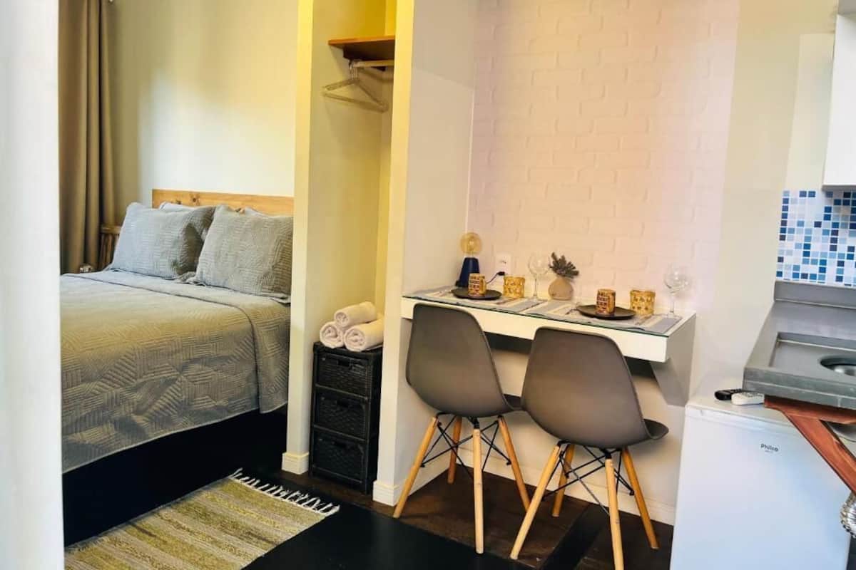 Habitación de hotel compacta con cama, un escritorio pequeño con dos sillas, un refrigerador y un salpicadero de azulejos.