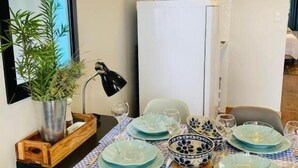 A dining area with a table set for four, a white refrigerator, a potted plant, and a mirror on the wall. - Pousada Maritimus (Barretos)