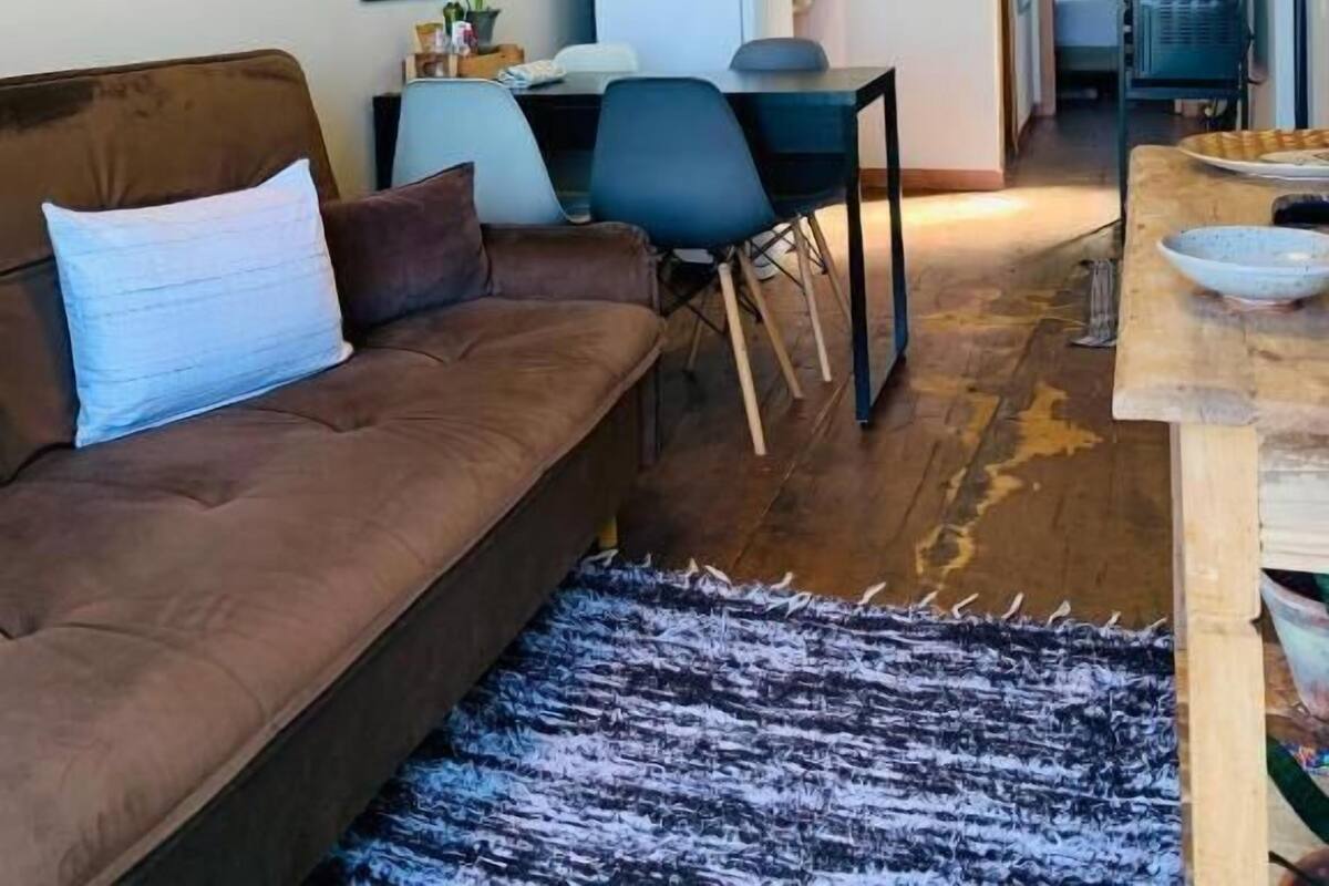 Una sala de estar moderna con un sofá marrón, una mesa de comedor con sillas y una cocina al fondo.