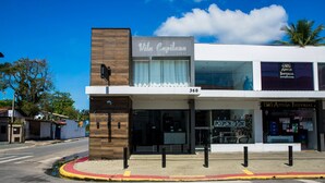 A modern building with a Vila Capilano sign, a storefront with ADEA Imperial branding, and a clear blue sky. - Loft c Smart TV e Wi-fi pr x ao Aqu rio de Ubatuba (Ubatuba)