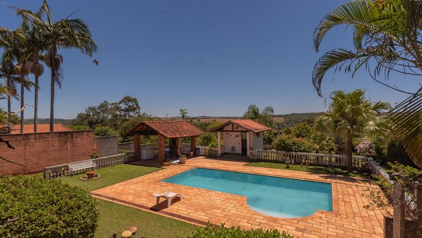 A swimming pool with a brick deck, surrounded by palm trees and a small gazebo. - Casa de Campo com Piscina e Lareira em Bragan a (Braganca Paulista)