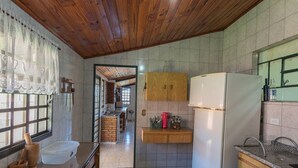 A kitchen with wooden cabinets, a refrigerator, and a window with lace curtains. - Casa de Campo com Piscina e Lareira em Bragan a (Braganca Paulista)