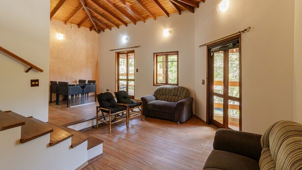A spacious living area with wooden flooring, a staircase, a sofa, and a dining table with chairs. - Casa com Piscina Sal o de Jogos e Churrasqueira (Mairipora)
