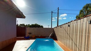 Ein rechteckiger Pool mit gefliestem Rand, umgeben von einer niedrigen Ziegelmauer und einem Holzzaun.