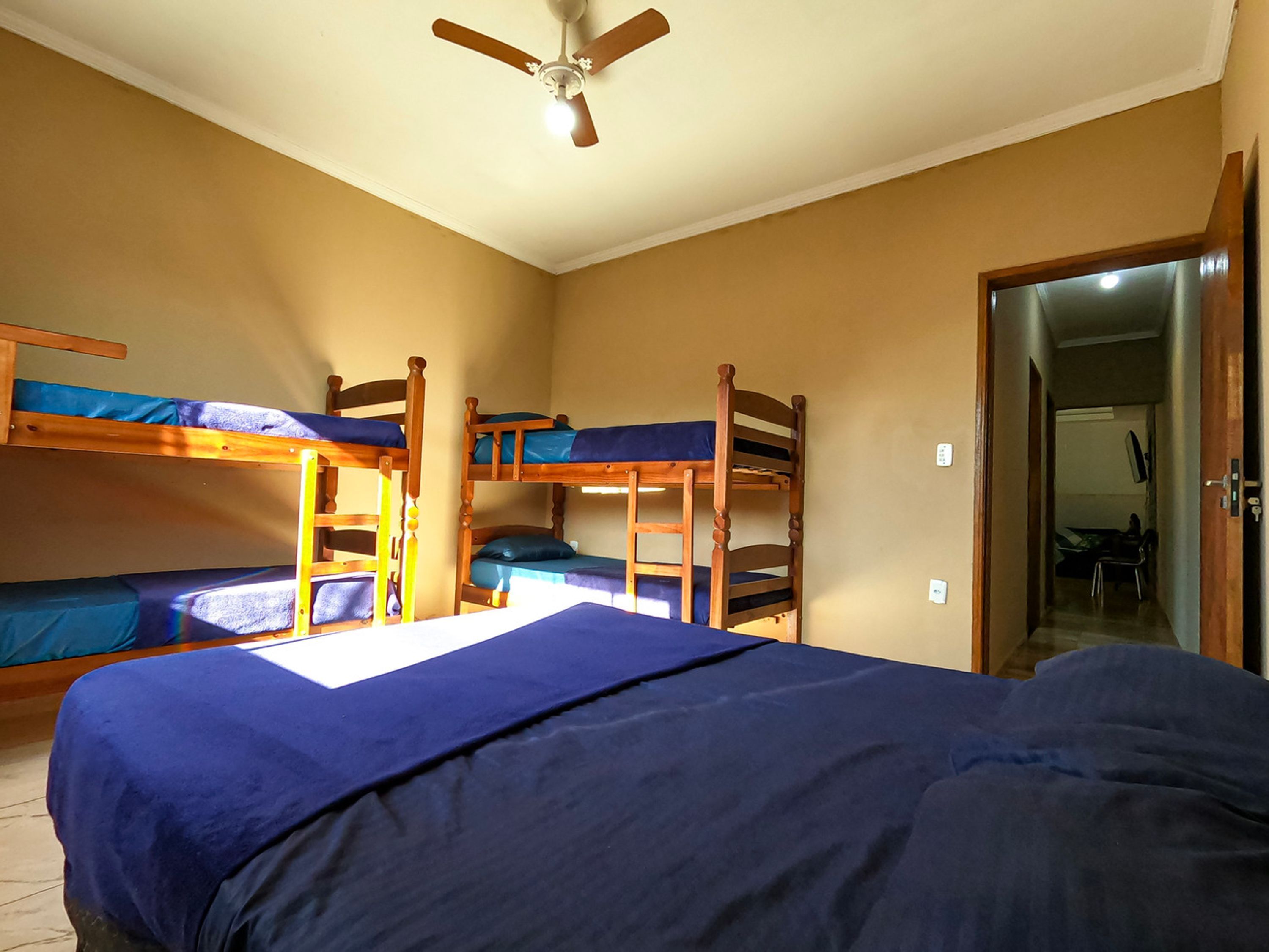 A dormitory room with bunk beds, a ceiling fan, and a door leading to another room.