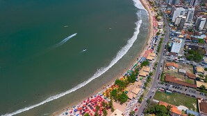 Vista aerea di una spiaggia con una fila di ombrelloni colorati e sedie a sdraio, accanto a una strada con edifici e automobili.