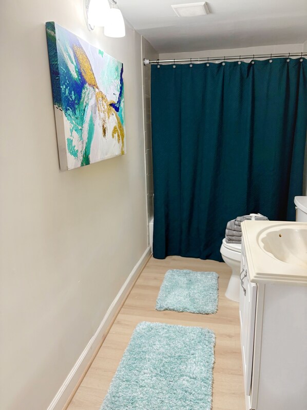 Un bagno con tenda doccia, lavandino e un quadro appeso al muro.