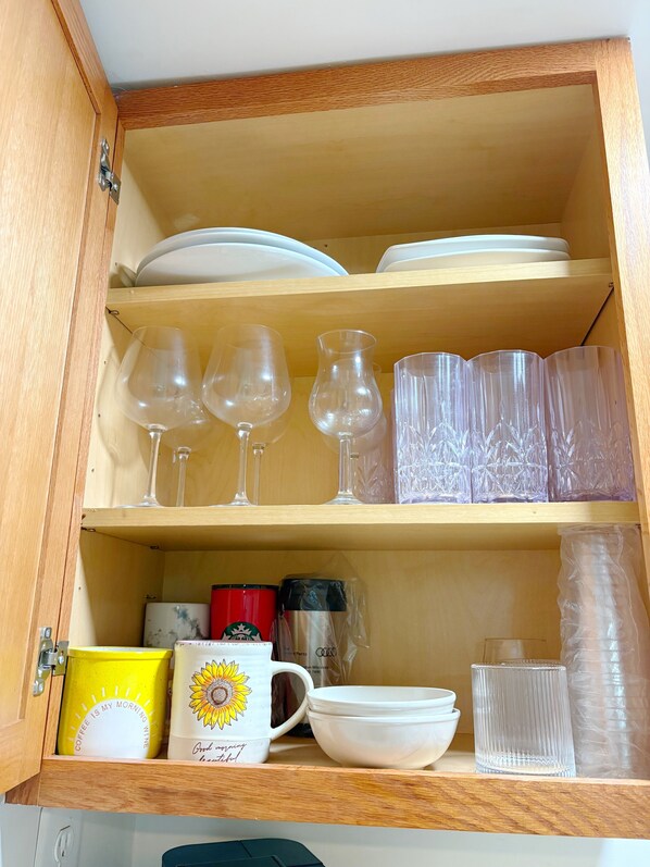 A wooden cabinet with shelves containing white plates, clear glassware, a yellow mug, and a white mug with a sunflower design. - Business-Ready Private Suite 15 minutes to DC Metro Area (Falls Church)