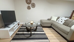 Een moderne woonkamer met een flatscreen televisie, een salontafel met glazen blad, een grijze bank en een zwart-wit gestreept vloerkleed.