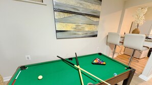 Een biljart met ballen en stokken, een schilderij aan de muur, en een zithoek met stoelen.