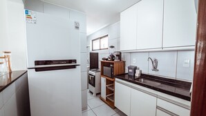 A modern kitchen with white cabinets, a black countertop, a refrigerator, a microwave, a stove, and a coffee maker. - Apartamento com Garagem a 200m da Praia do Bessa (João Pessoa)