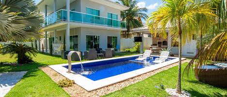 A modern two-story house with a swimming pool, outdoor seating, and palm trees.