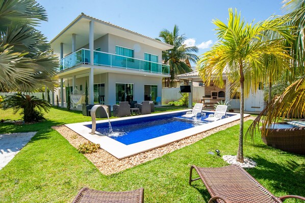 A modern two-story house with a swimming pool, outdoor seating, and palm trees. - Casa com Piscina Quadra de Areia e Churrasqueira (Araruama)