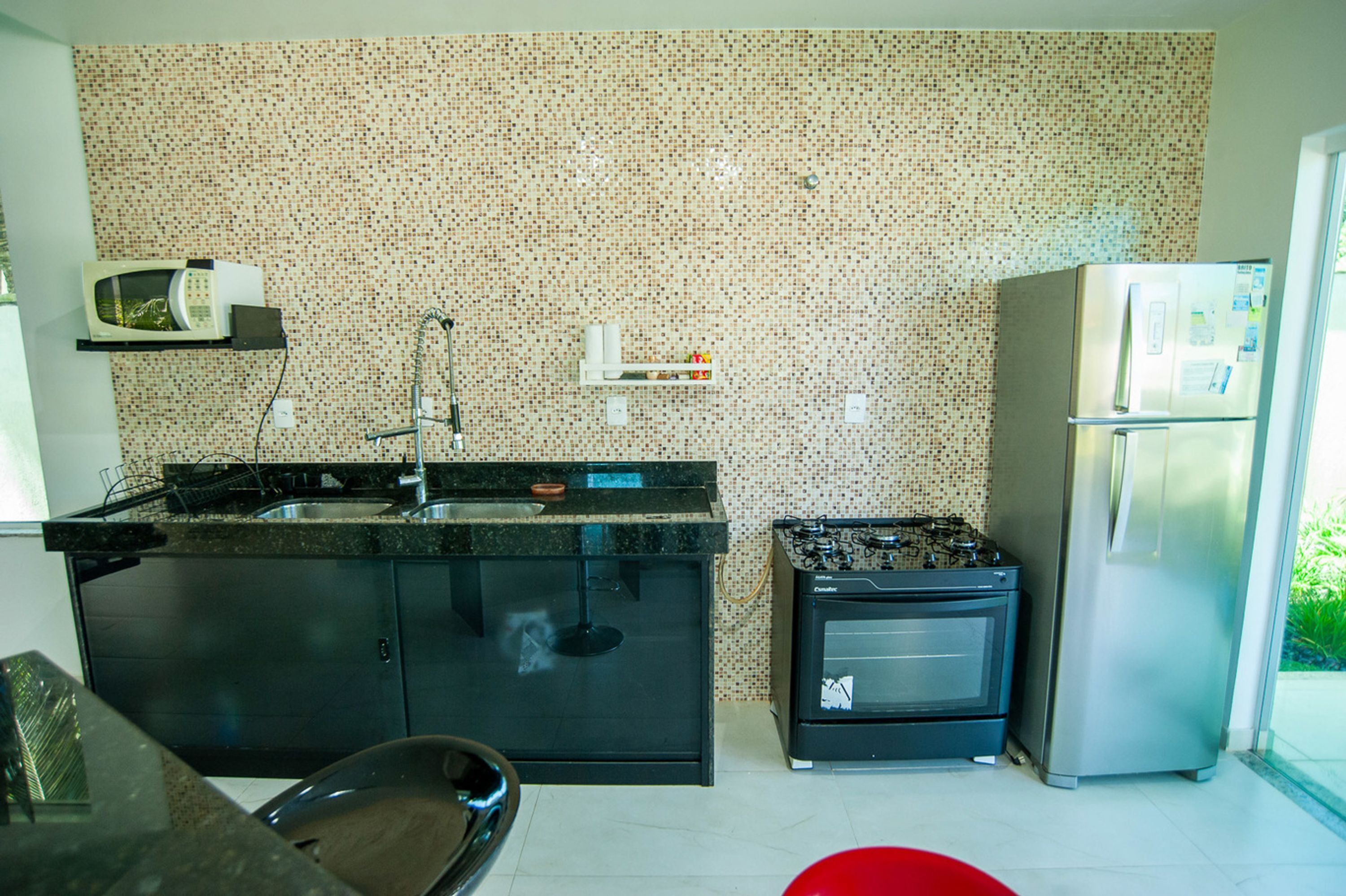 A kitchen with a black countertop, a stove, a microwave, and a refrigerator.