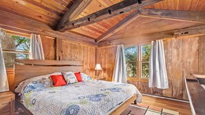 A wooden cabin bedroom with a bed, curtains, and a window.