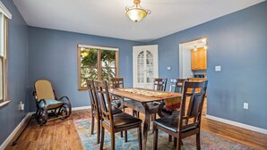 A dining room with a wooden table and chairs, a wheelchair, and a patterned rug.