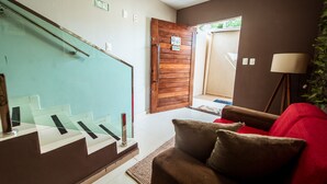 A living room with a staircase, a wooden door, and a red sofa. - Casa em Jacum com Piscina 5 Suites e Fliperama (Conde)
