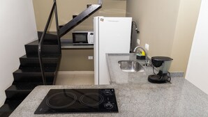 A compact kitchen with a built-in stove, a microwave, a refrigerator, a sink, and a small countertop. - Loft c Ar Smart Lock e Wi-fi no Cora o do Itagu (Ubatuba)