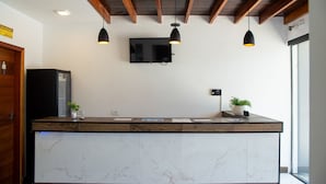 A kitchen with a marble island, wooden beams, pendant lights, a flat-screen TV, and a refrigerator. - Loft com Wi-fi e Smart Lock Perto do Projeto Tamar (Ubatuba)