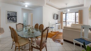A dining area with a glass table, wicker chairs, and a cowhide rug. - Apartamento com Varanda Churrasqueira e Vista Mar (Itapema)