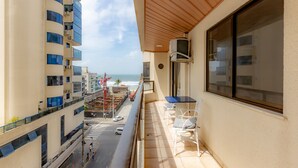 A balcony with a view of the ocean and a cityscape, featuring a table and chairs. - Apartamento com Varanda Churrasqueira e Vista Mar (Itapema)