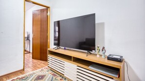 A living room with a large flat-screen TV on a wooden stand, a patterned rug, and a small figurine on the stand. - Apartamento c Fechadura Eletr Nica a 200m do Metr (São Paulo)