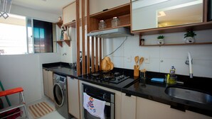 A modern kitchen with a built-in washer, oven, and stove. There are wooden shelves, a window, and a sink. - Apto com Piscina e Garagem em Barra dos Coqueiros (Barra dos Coqueiros)