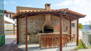 An outdoor brick oven with bar stools and a covered seating area. - Apto com Piscina e Garagem em Barra dos Coqueiros (Barra dos Coqueiros)