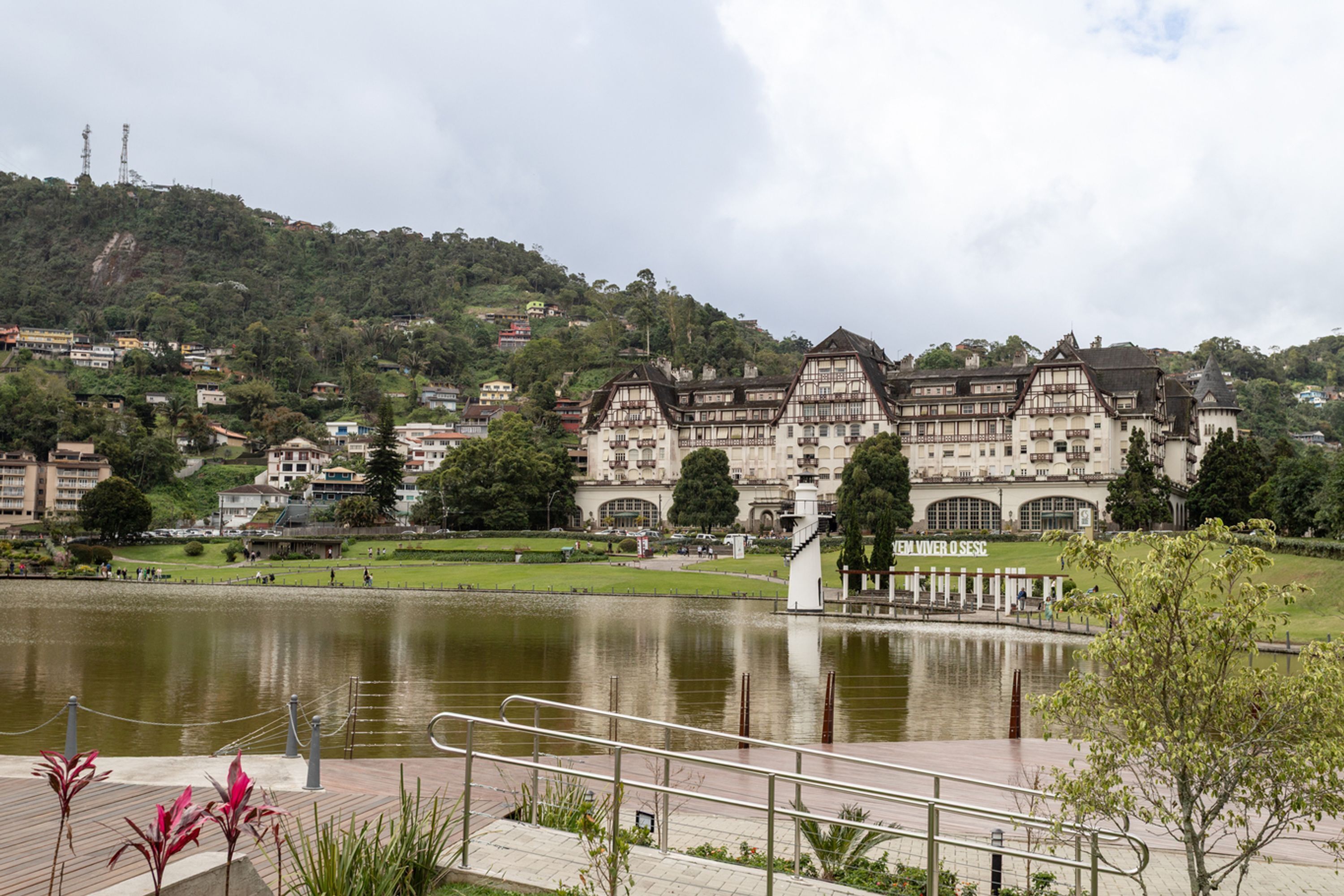 A historic building with a large pond in front, surrounded by greenery and hills.